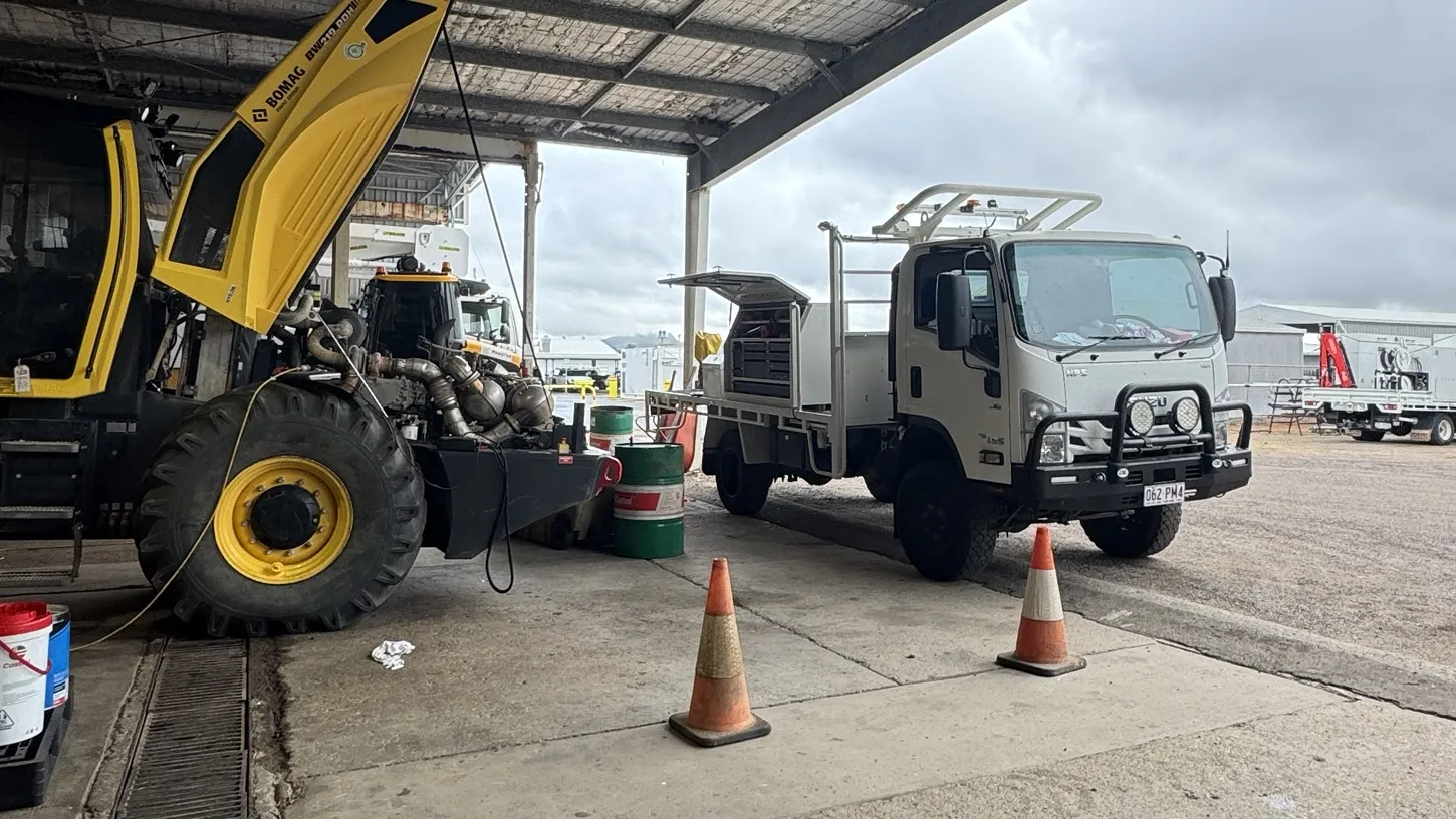Bomag roller with the engine cover up under a shed, 12Mech service truck alongside